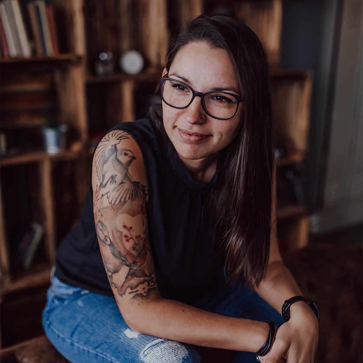 Kerstin Partheder Design & Illustration, Grafikerin aus Linz, sitzend, lächelnd mit Tatowierung auf rechtem Arm